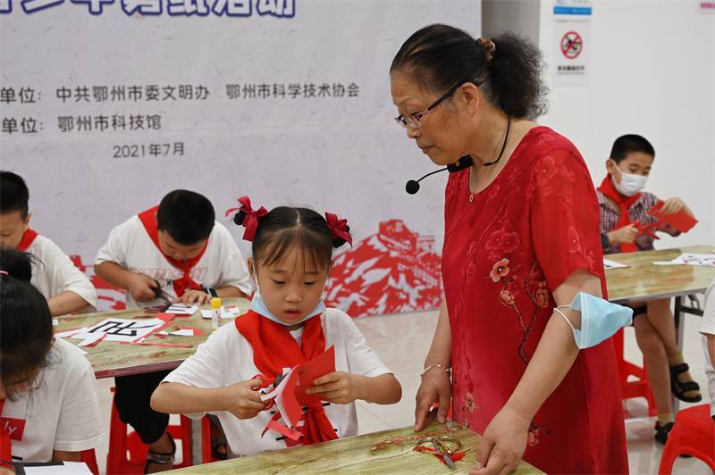 2021年7月10日，鄂州市科協(xié)組織落駕坪小學(xué)學(xué)生在鄂州市科技館開展社會(huì)主義核心價(jià)值觀系列活動(dòng)，圖為開展的紅色剪影圓夢中華剪紙活動(dòng)，老師指導(dǎo)同學(xué)剪紙.jpg